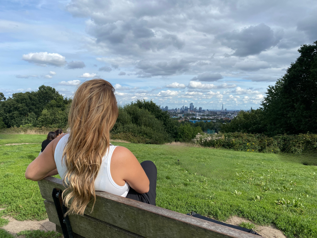 A girl sitting on a bench during the pretty little london tour. She is watching London park.